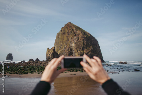 Mobile phone and hands taking photo of Haystack Rock.