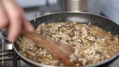 Close-up of mixing with a wooden spoon mushroom risotto. Concept of preparing mushroom risotto with vegetable stock in a pan in 4k