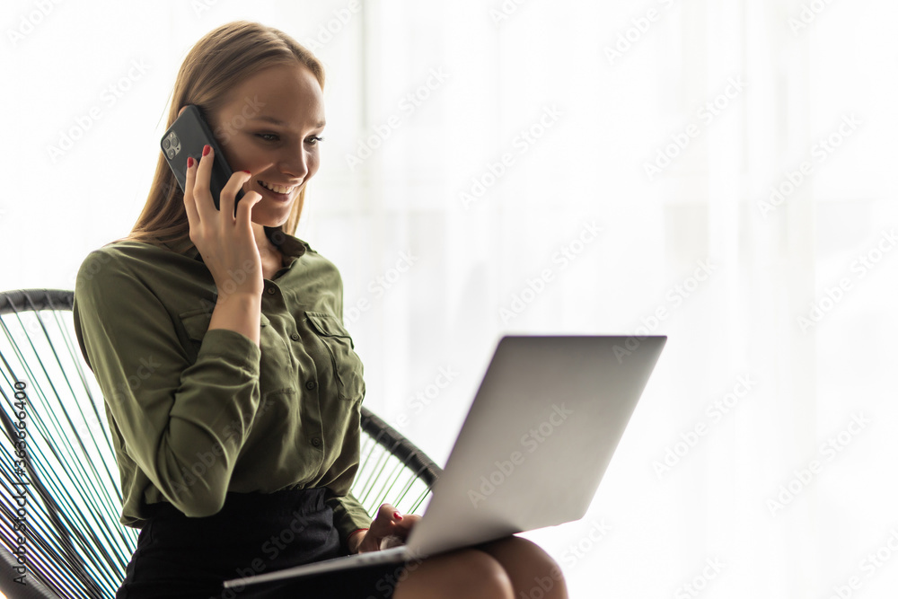 Smiling young business woman sitting by the table and talking on phone in office Smiling young business woman sitting by the table and talking on phone in office