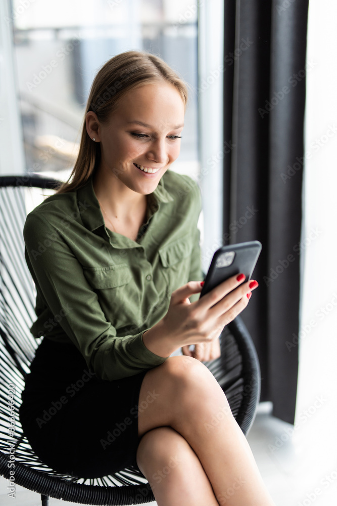 Time to relax. Calm girl networking on smartphone, sitting in chair near window