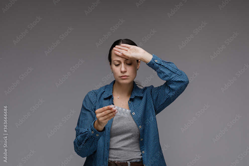 Young woman holds prescribed pills in her hand, feeling ill, gray background Young woman holds prescribed pills in her hand, feeling ill, gray background