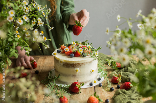 On the table is a cake decorated with flowers and berries