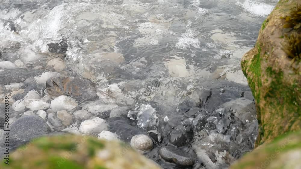 Ocean waves washing over rocky pebble shoreline close up dolly right Ocean waves washing over rocky pebble shoreline close up dolly right