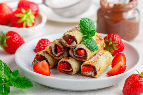 Rolls with chocolate and nut filling (Nutella), fresh strawberry berries, powdered sugar and mint. Delicious gourmet Breakfast. Selective focus