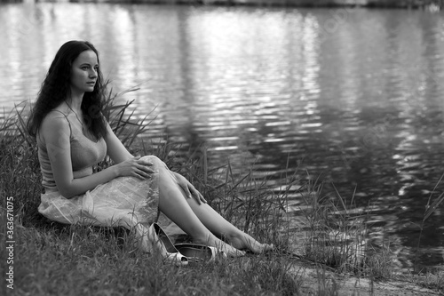 Black and white photography of curly woman sitting on the grass near the lake