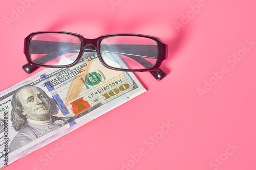 Banknote of one hundred dollars near glasses on pink background. Financial concept
