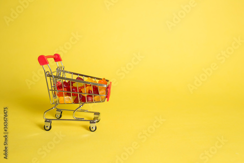 Metal cart with marmalade in the shape of bears on a yellow isolated background with space for text