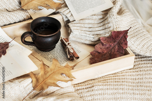 Autumn, fall leaves, a hot steaming cup of coffee and a warm sweater on a wooden tray. Seasonal, morning coffee, sunday relaxation and still life concept.