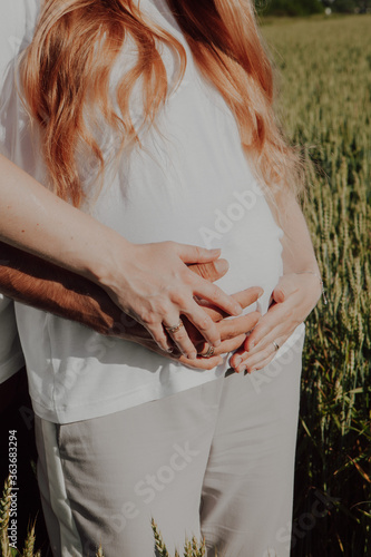 A pregnant woman and her husband and baby daddy-to-be holds hands on her stomach hugs his wife. Close-up of arms and abdomen. Pregnancy women