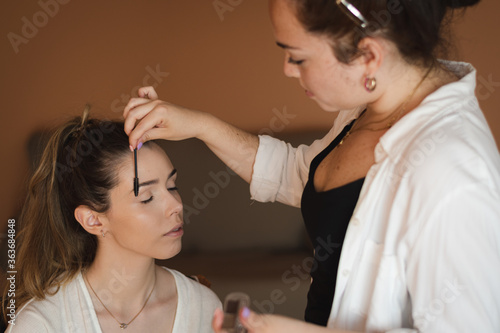Make-up artist applying makeup to a young blonde model with her hair up. Makeup with brushes on the face in a makeup studio