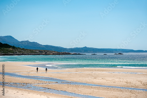 seascape of a beach in the atlantic ocean with fine sand and small silhouettes of people walking