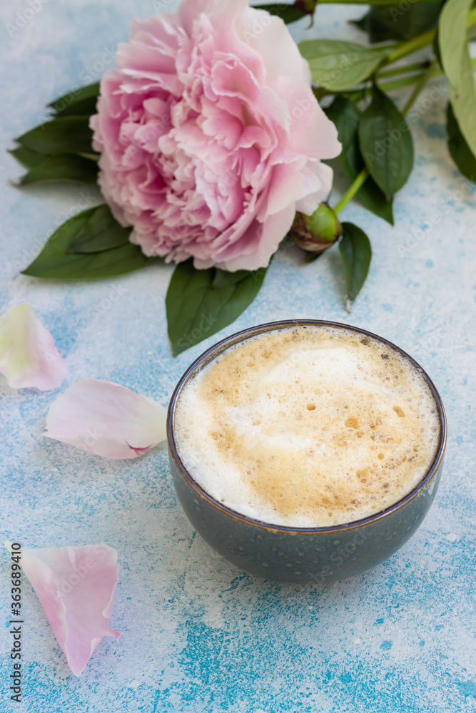 Morning cup of coffee or cappuccino and pink peonies on blue concrete table. Creative breakfast for Woman or Mother day. Morning cup of coffee or cappuccino and pink peonies on blue concrete table. Creative breakfast for Woman or Mother day.
