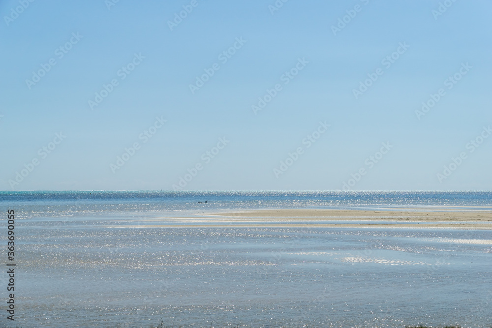 Minimalist seascape with blue ocean and sandbank on a sunny day. Sky is clear blue