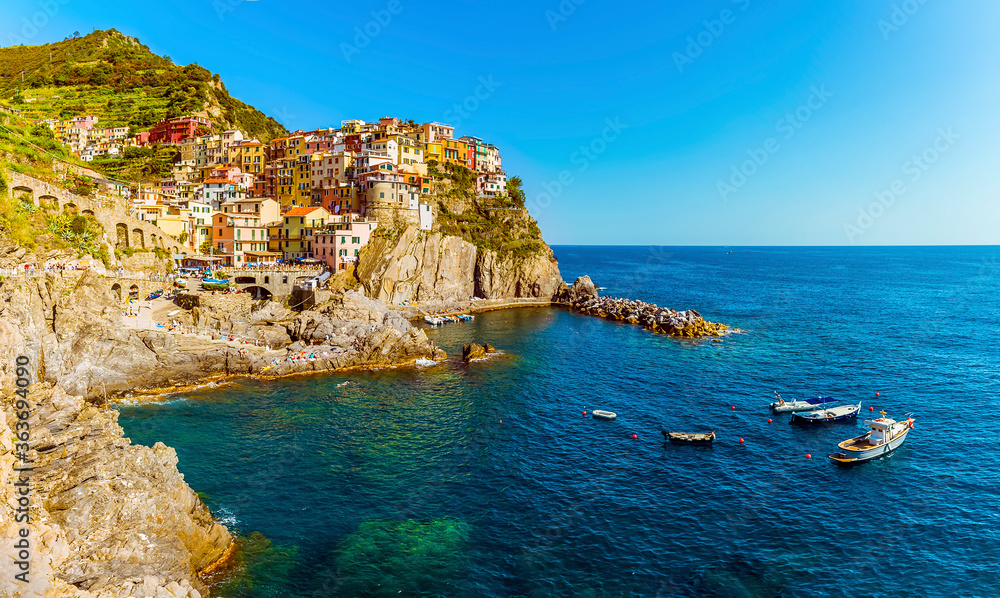 A panorama view across the rocky coastline towards the village of Manarola, Cinque Terre, Italy in the summertime