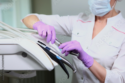 A nurse in uniform and a medical mask wipes the dental unit. Gloved hand.Disinfection in the dental office. Copy of the space. Gray background.