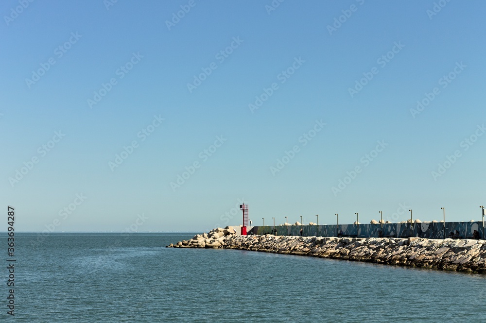 The pier of Pesaro harbor with breakwater cliffs, a colored wall and a small red lighthouse (Marche, Italy, Europe)