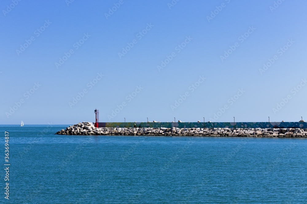 The pier of Pesaro harbor with breakwater cliffs, a colored wall and a small red lighthouse (Marche, Italy, Europe)