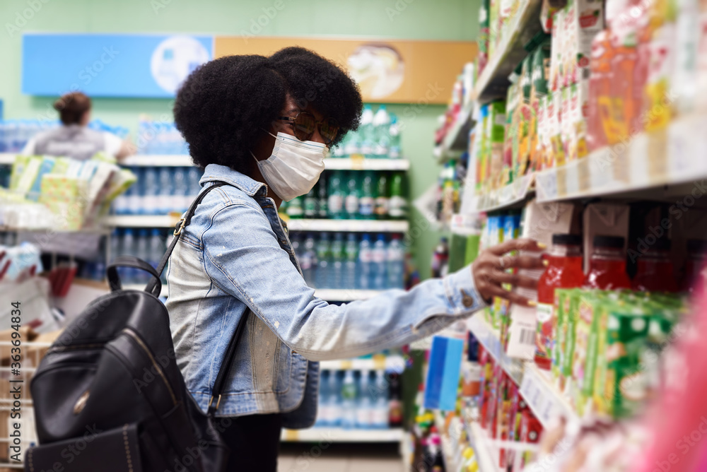A dark-skinned girl chooses products in a protective mask. The concept of the coronavirus pandemic and virus protection