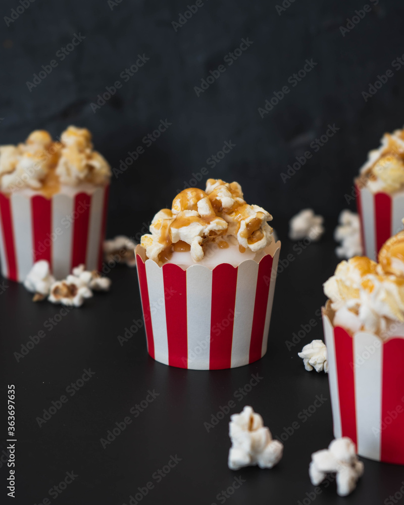 Vanilla frosted cupcakes topped with popcorn and salted caramel sauce arranged against a black background with copy text space.