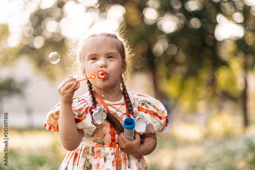 A girl with Down syndrome blows bubbles. The daily life of a child with disabilities. Chromosomal genetic disorder in a child. photo