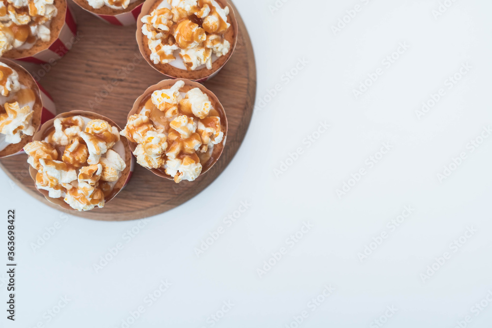 A flat lay style image with salted caramel popcorn vanilla frosted cupcakes arranged in a circular fashion in the top left corner of the image. Plain white background with copy text space A flat lay style image with salted caramel popcorn vanilla frosted cupcakes arranged in a circular fashion in the top left corner of the image. Plain white background with copy text space
