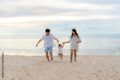 Happy Asian family holidays during joyful father, mother and daughter running together along summer sunset sea. Happy family travel on beach in holiday, Summer and vacation.