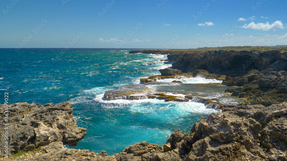 Cinematic shot of emerald colored ocean waves crashing into distant cliffs.