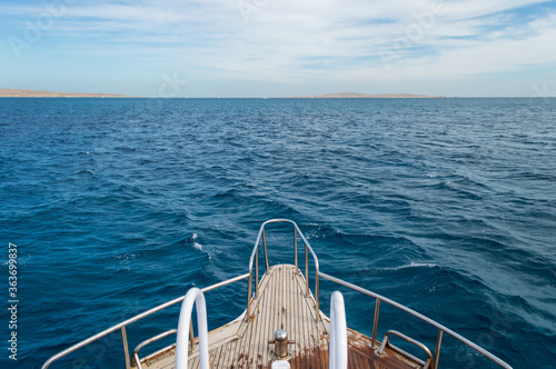 Bow of yacht on seascape background. View from yacht bow to sea horizon. Blue waves of Red sea. Way to horizon. Cloudy sky.