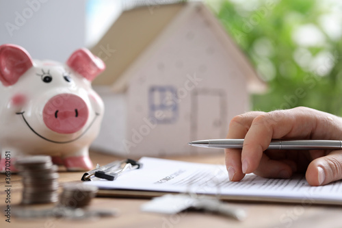 Man fills in lease document at home, on piggy bank photo