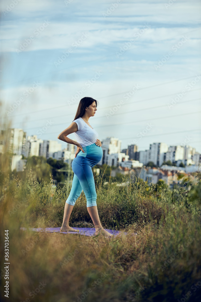 Pregnant woman doing yoga outdoors.