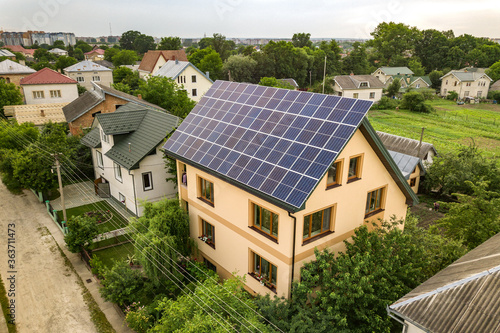 Aerial top view of new modern residential house cottage with blue shiny solar photo voltaic panels system on roof. Renewable ecological green energy production concept. © bilanol