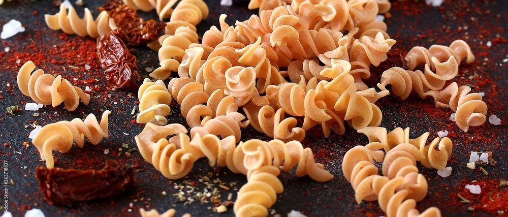 raw fusilli paprika pasta, close-up on a black background. homemade pasta without dyes from durum wheat. raw fusilli paprika pasta, close-up on a black background. homemade pasta without dyes from durum wheat.