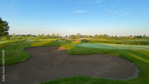 Fototapeta Naklejka Na Ścianę i Meble -  sunrise on golf course golf green flag pole sand trap morning moon