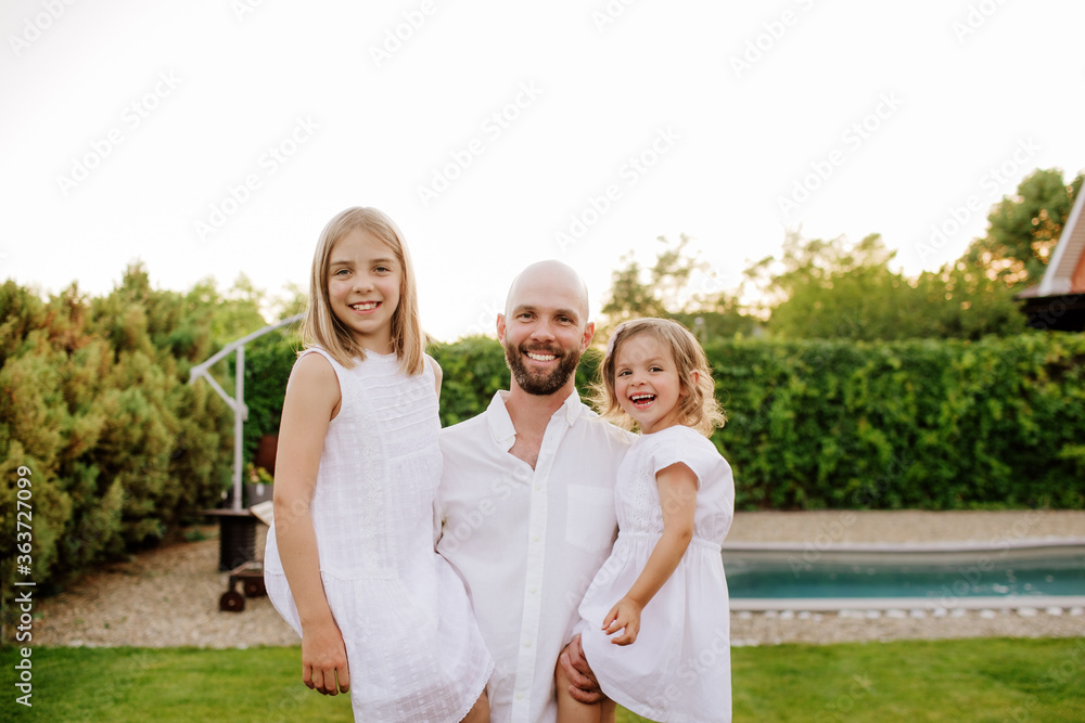 a father holds two blonde daughters in white clothes in his arms a father holds two blonde daughters in white clothes in his arms