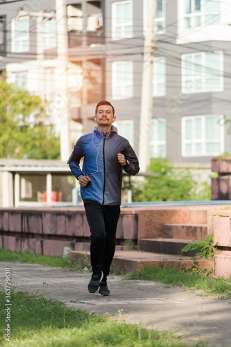 An athletic man in sport hoodie jogging in the city park in the evening after stressful work.