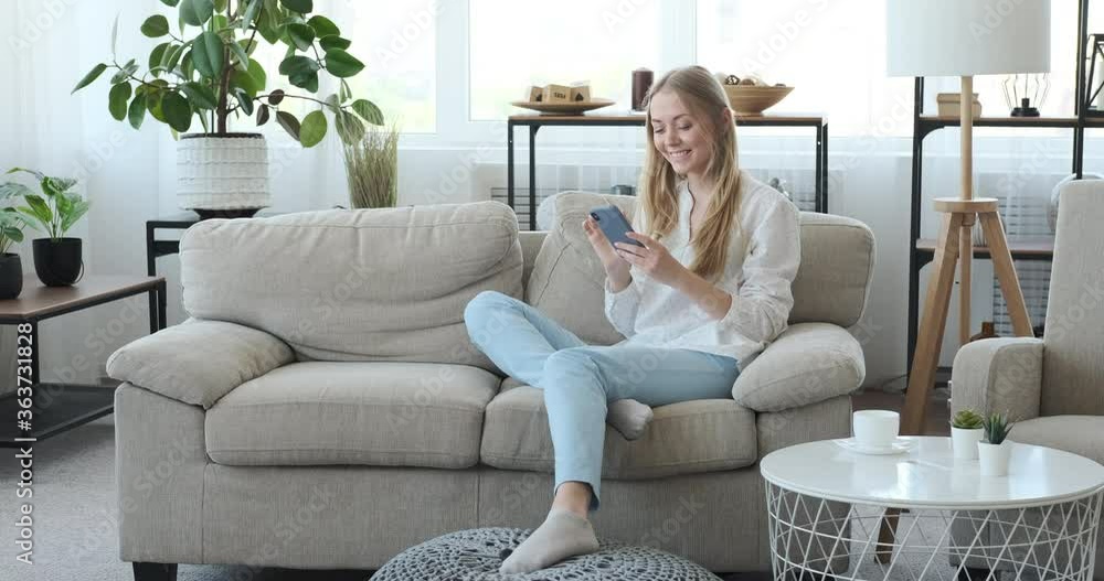 Woman having fun text messaging using mobile phone on sofa at home Woman having fun text messaging using mobile phone on sofa at home