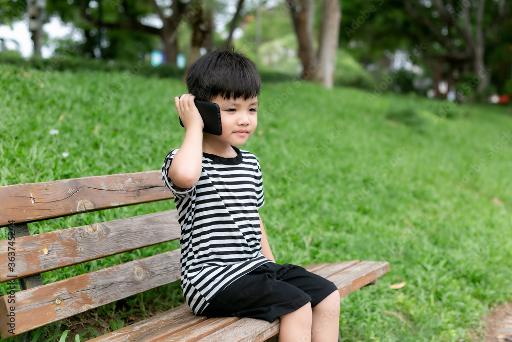 Cute little boy sitting on a park bench and playing with mobile phone Cute little boy sitting on a park bench and playing with mobile phone
