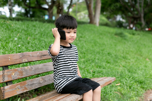 Cute little boy sitting on a park bench and playing with mobile phone