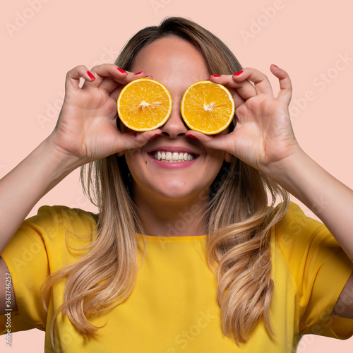 Happy and smiling young man playing with an orange cut in half and in front of his eyes. Photo on solid color background.