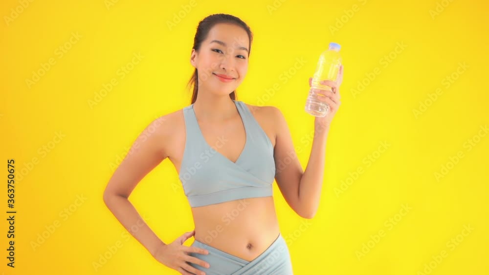 Beautiful happy asian woman in sport suit showing bottle of water to camera, full frame slow motion. Isolated on yellow background Beautiful happy asian woman in sport suit showing bottle of water to camera, full frame slow motion. Isolated on yellow background