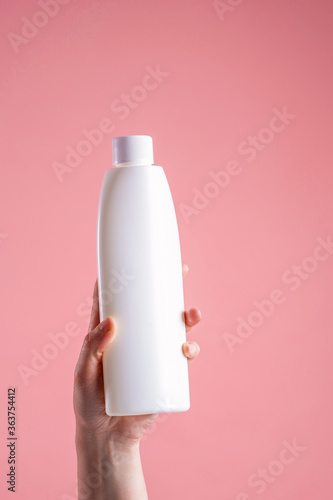 Close-up woman s hand holding tool  household chemicals  on a pink background.