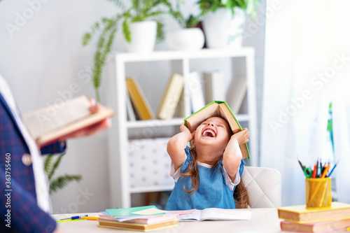 little girl engaged in lessons with teacher at home, fools around and laughs. photo