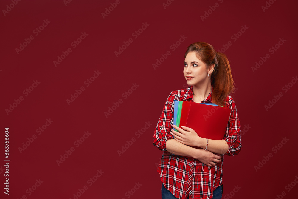 Teen student girl isolated on a red background holding folders for study Teen student girl isolated on a red background holding folders for study