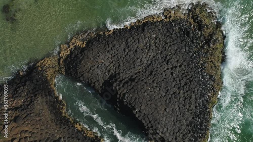 Aerial view of basalt, volcanic rock formation with ocean waves, 50% speed slow motion.