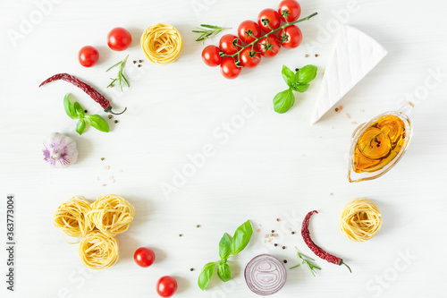 Frame of italian pasta ingredients for cooking. Raw pasta, cheese, vegetables, spices and herbs top view on white wooden background.