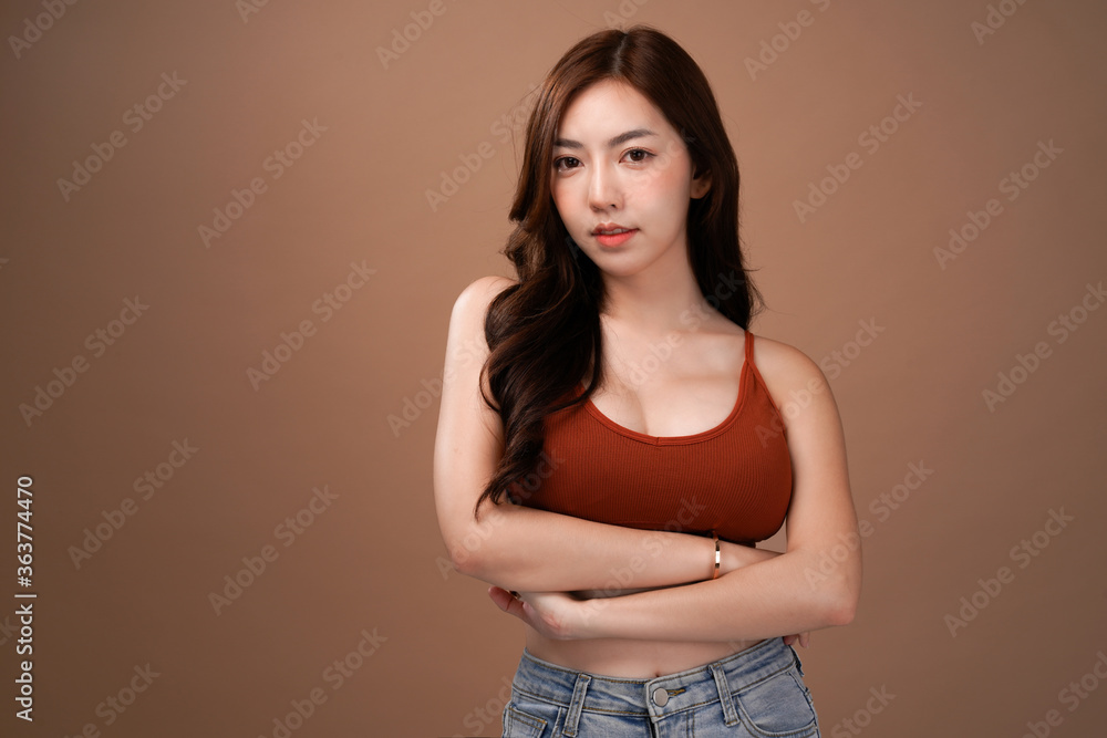 Obraz premium Slim body and big breast asian woman standing and crossed arm, Red crop bralette outfit, isolated with mocha brown background