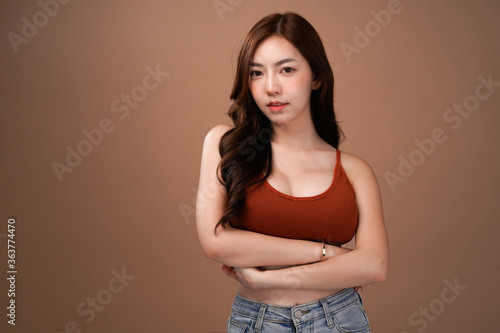 Slim body and big breast asian woman standing and crossed arm, Red crop bralette outfit, isolated with mocha brown background