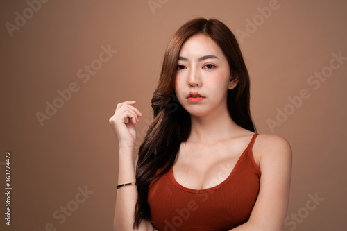 Slim body and big breast asian woman standing and crossed arm, Red crop bralette outfit, isolated with mocha brown background