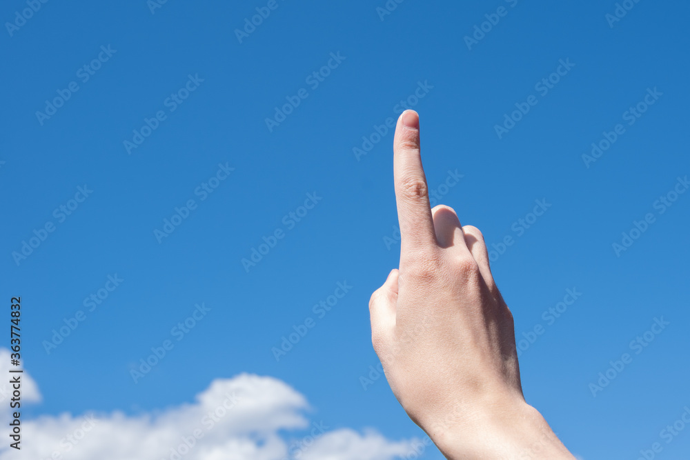 Close-up female hand with index finger up on a background of blue sky with clouds, copy space Close-up female hand with index finger up on a background of blue sky with clouds, copy space