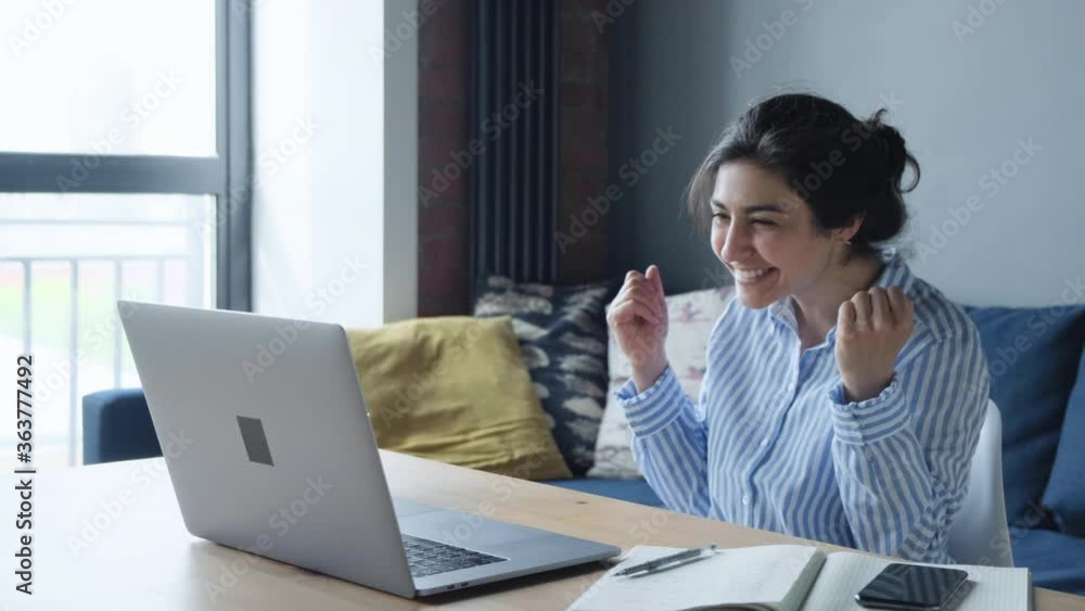 Young successful indian woman celebrate victory triumph looking at laptop Girl is Happy and Smiling, she Works at the Computer at Home Young successful indian woman celebrate victory triumph looking at laptop Girl is Happy and Smiling, she Works at the Computer at Home